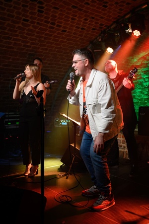 Koncert S.M.ROCK: na scenie nauczyciele śpiewu Weronika Kukla i Sławomir Ramian, w tle nauczyciel gry na basie Grzegorz Nosek podczas wykonania piosenki