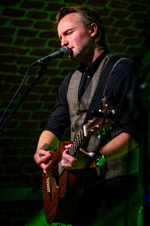 Koncert: Zaduszki - Scena w Piwnicach TCK. Kamil Juszczyk śpiewa i gra na gitarze akustycznej.