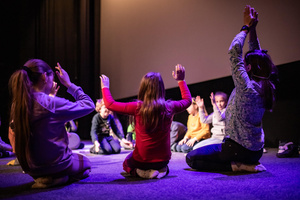 Filmowe ferie w kinie Marzenie - Na fotografii widzimy grupę dzieci siedzących w półkolu na scenie przed ekranem, podczas animacji poprzedzających projekcje filmowe w ramach cyklu "Filmowe ferie".