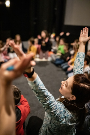Filmowe ferie w kinie Marzenie - Na fotografii widzimy grupę dzieci siedzących w półkolu na scenie przed ekranem, podczas animacji poprzedzających projekcje filmowe w ramach cyklu "Filmowe ferie".
