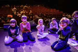 Filmowe ferie w kinie Marzenie - Na fotografii widzimy grupę dzieci siedzących w półkolu na scenie przed ekranem, podczas animacji poprzedzających projekcje filmowe w ramach cyklu "Filmowe ferie".