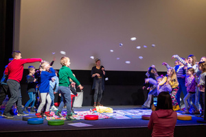 Filmowe ferie w kinie Marzenie - Na fotografii widzimy grupę dzieci na scenie przed ekranem, podczas animacji poprzedzających projekcje filmowe w ramach cyklu "Filmowe ferie".