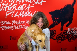 38. TNF - Dzień 6 (5.06.2024) - Reżyserka "Imago" Olga Chajdas z suczką Nioki na rękach na tle ścianki festiwalowej w Marzeniu