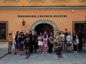 Wakacje z otwARTą: Kurs rysunku i malarstwa - Grupa uczestników warsztatów podczas pamiątkowego zdjęcia przed wejściem do Tarnowskiego Centrum Kultury.