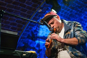 Koncert: Pracownia Piosenki "Na przekór" - Podczas koncertu. Na scenie Sławek Ramian gra na flecie.