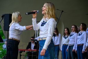 Koncert Chóralne Majówki: Chór Fox Vox - Na amfiteatralnej scenie na pierwszym planie śpiewająca solistka, w tle chór Fox Vox
