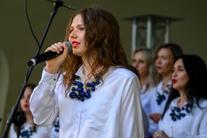 Koncert Chóralne Majówki: Chór Fox Vox - Na amfiteatralnej scenie na pierwszym planie śpiewająca solistka, w tle chór Fox Vox