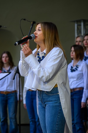 Koncert Chóralne Majówki: Chór Fox Vox - Na amfiteatralnej scenie na pierwszym planie śpiewająca solistka, w tle chór Fox Vox