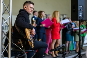 Koncert Chóralne Majówki: Chór SOLski - Na scenie na pierwszym planie grający  basista Michał Kołodziej, w tle śpiewający chórzyści