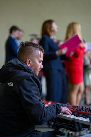 Koncert Chóralne Majówki: Chór SOLski - Na scenie na pierwszym planie grający  pianista Piotr Niedojadło, w tle śpiewający chórzyści