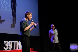 39. TNF: Dzień 4 (2.06.2025) - Na scenie Marzenia Damian Kocur, reżyser filmu "Pod wulkanem" zapraszający widzów na projekcję. W tle Kuba Armata