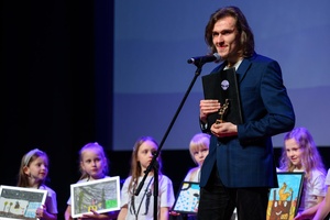 39. TNF: Gala Wręczenia Nagród (7.06.2025) - Na scenie laureat FMW Damian Tchórzewski przemawiający do publiczności, w tle Jury Dziecięce ze swoimi plastycznymi pracami dla laureata Filmów Młodego Widza