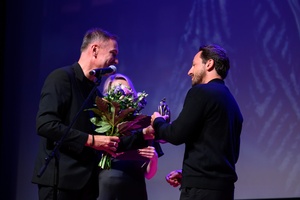 39. TNF: Gala Wręczenia Nagród (7.06.2025) - Na scenie dyr. TCK Tomasz Kapturkiewicz i jego zastępczyni Dominika Dąbek wręczający Tadeuszowi Śliwie reżyserowi "Światłoczułej" statuetki Publika i kwiaty